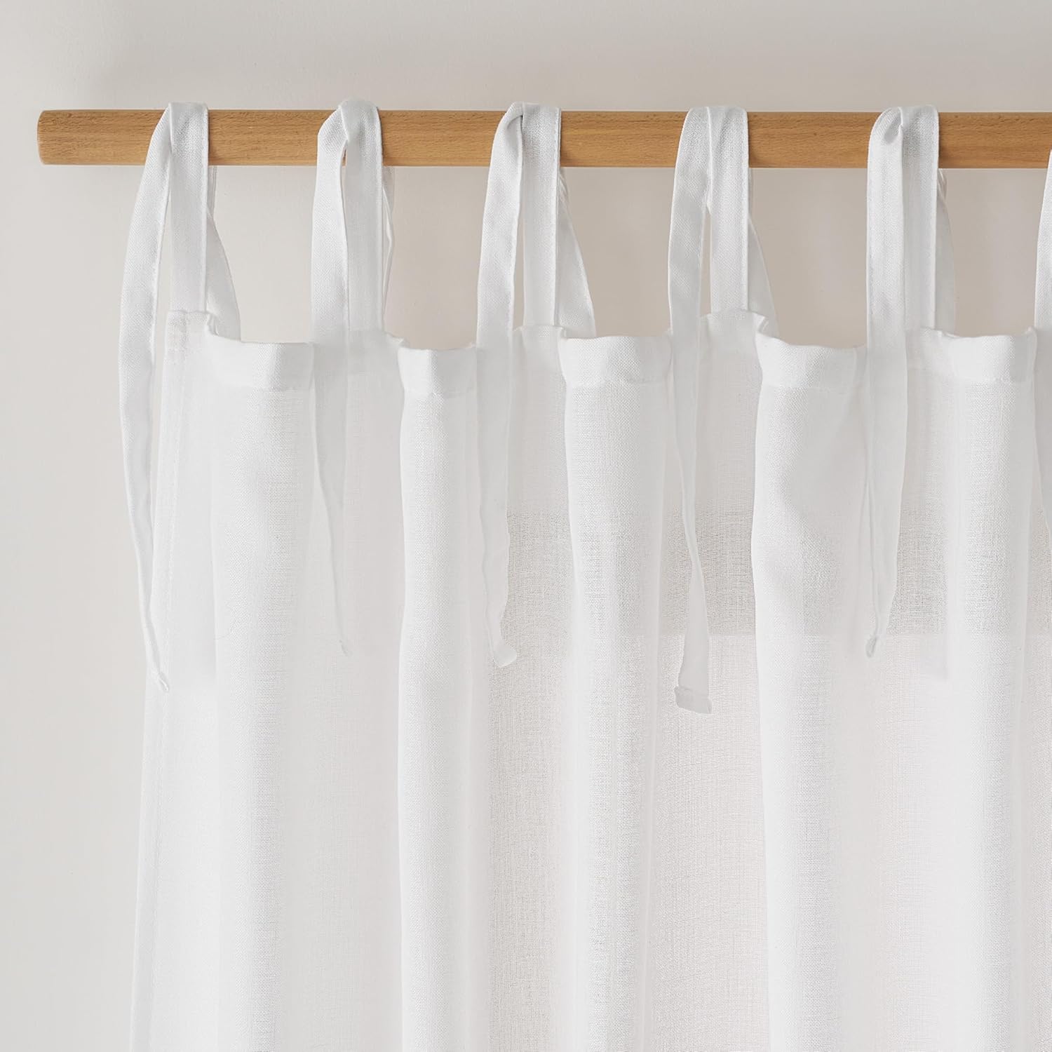 White linen tie-top sheer curtains with visible texture hanging on a natural wooden rod.