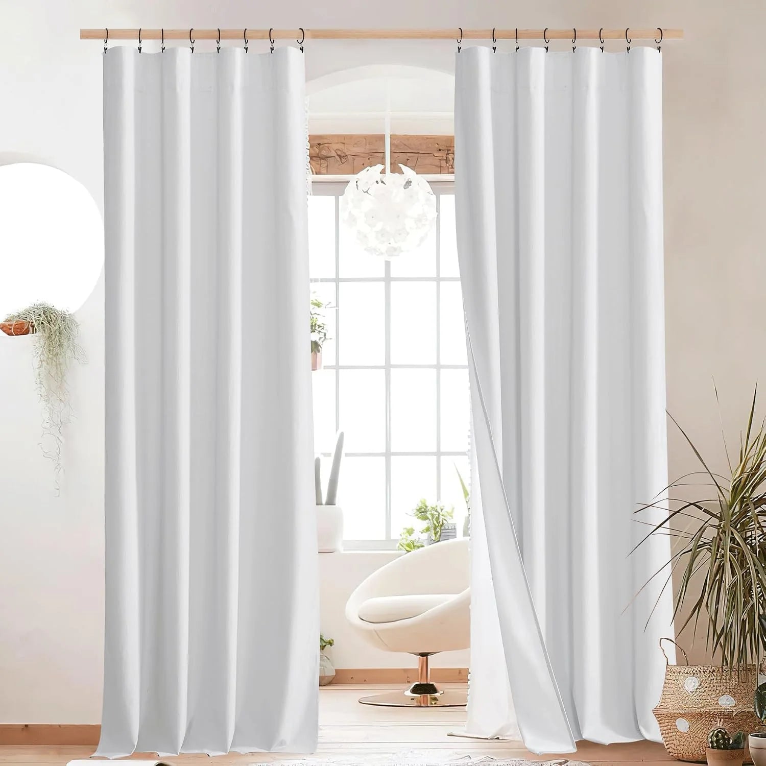 White floor-length curtains with black ring hooks on a wooden rod in a bright minimalist room