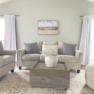 White opaque rod-pocket curtains on black rods frame windows in a modern living room with light beige sofa.