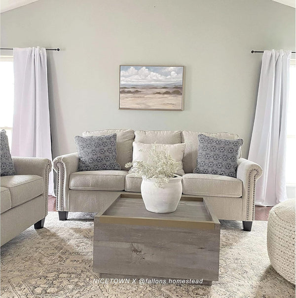 White opaque rod-pocket curtains on black rods frame windows in a modern living room with light beige sofa.