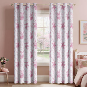 White curtains with pink floral pattern and grommet top, hanging on a gold rod in a bright bedroom.
