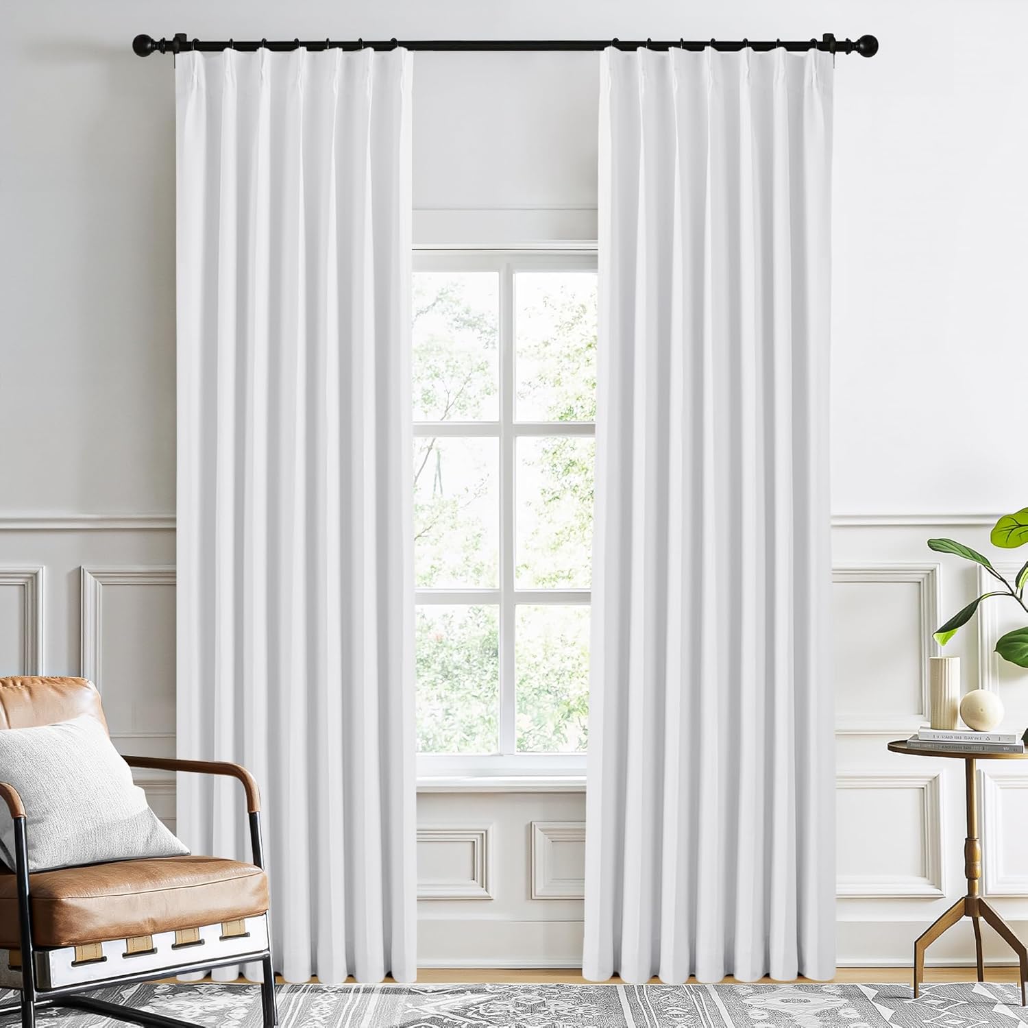 Two pure white pleated curtains with deep folds hanging on a black rod in a bright living room.
