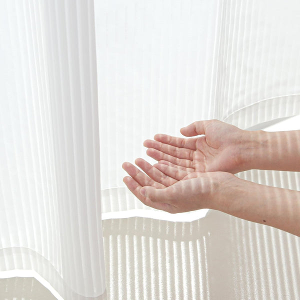 White pleated translucent curtain. Hands demonstrate light filtering effect and vertical striped shadows.