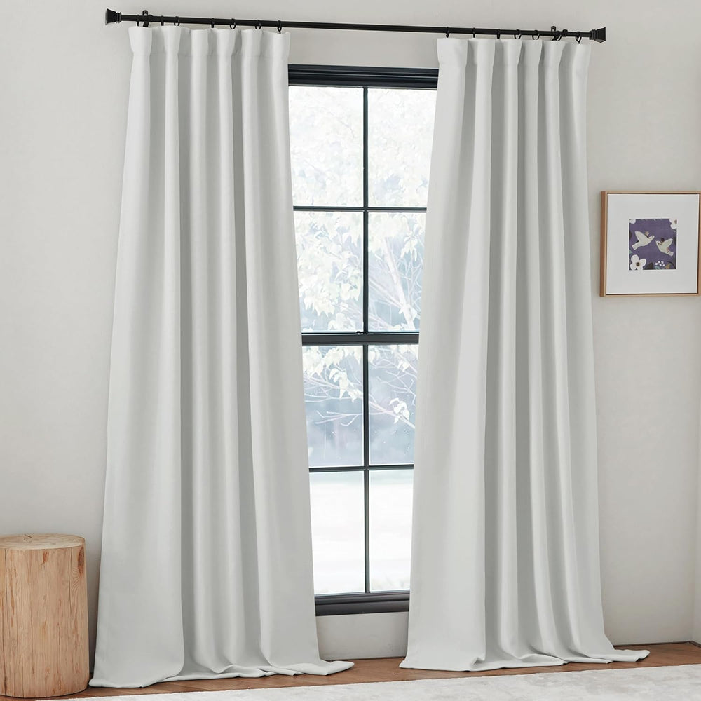 Long white pleated curtains hanging on a black rod, offering elegant room darkening for a modern window.