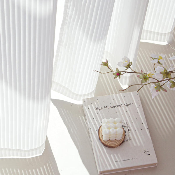 White pleated sheer curtains with sunlight casting striped shadows.