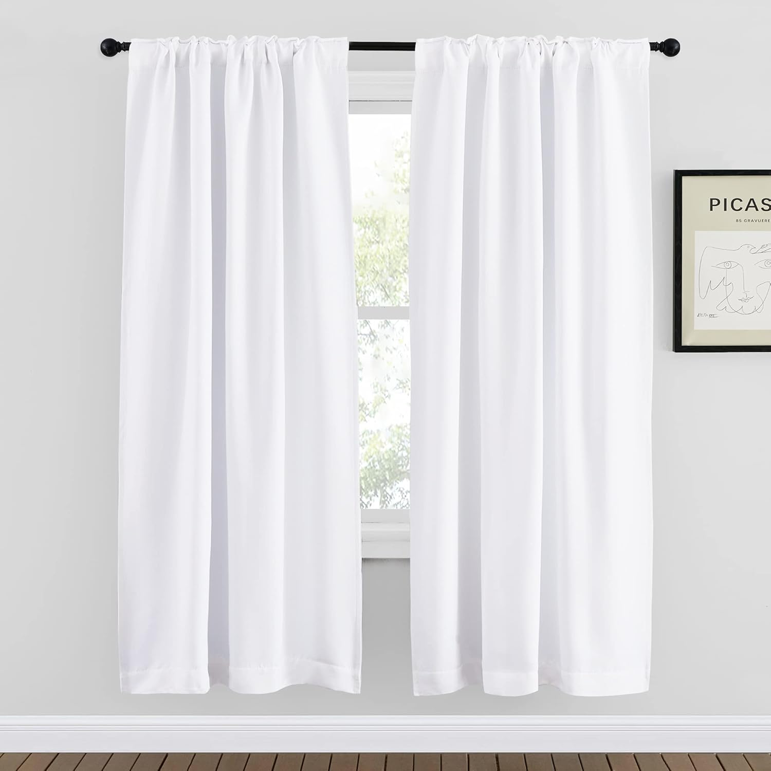 Pair of white rod pocket curtains on a black rod, filtering light from a window in a modern room.