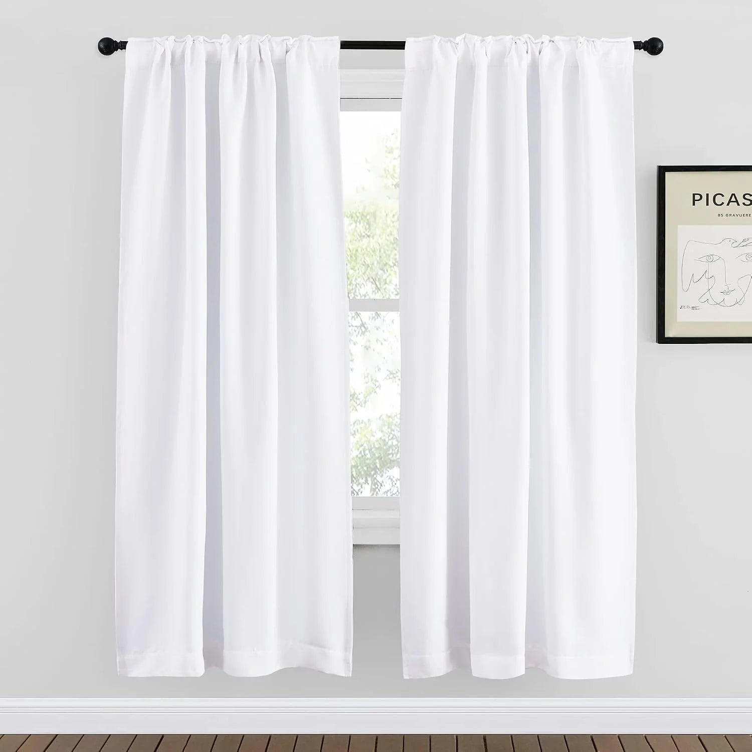 White rod pocket curtains hanging on a black curtain rod in a bright minimalist room