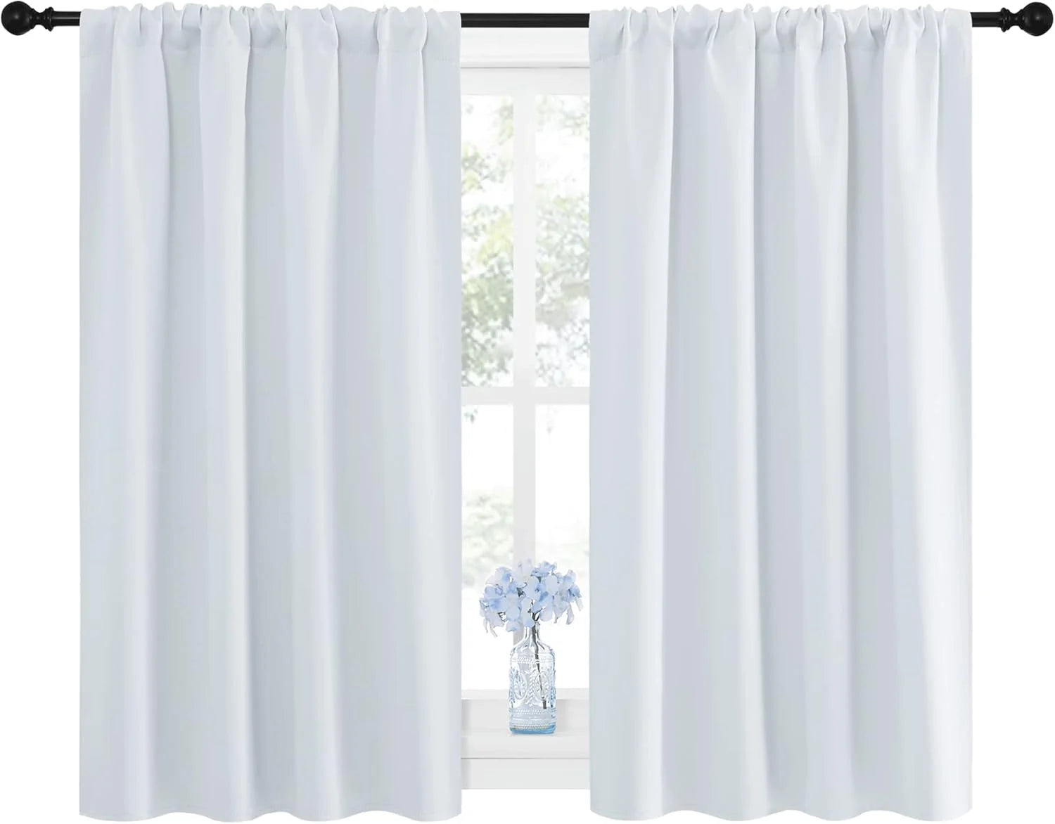 Pair of white rod pocket curtains hanging on a black rod in front of a bright window with blue flowers.