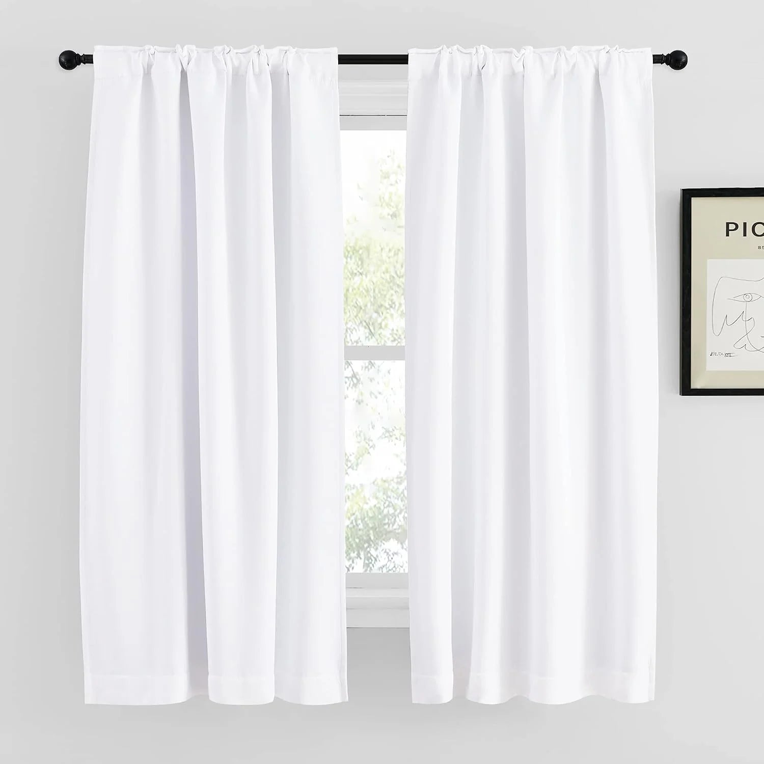 White rod pocket curtains hanging on a black curtain rod over a bright window