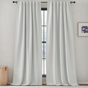 White room darkening rod pocket drapes hang on a black rod over a window, pooling on the floor.