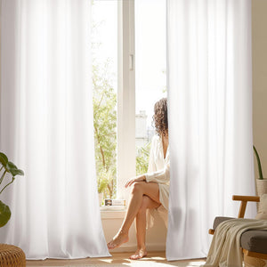 Bright white room darkening window curtains with a soft drape, partially drawn in a sunlit room.