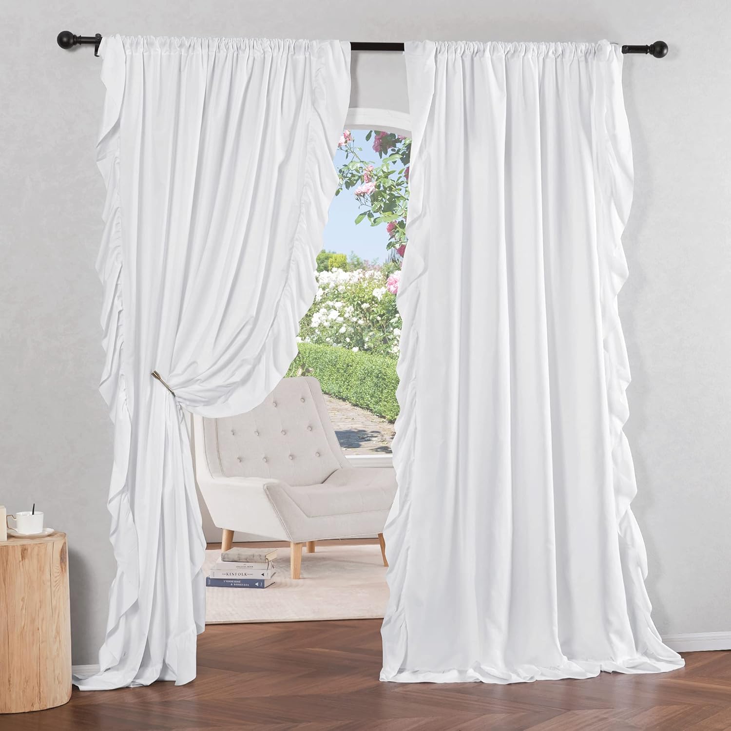 White ruffled curtains with rod pocket top. One panel tied back. Soft fabric frames a garden view.