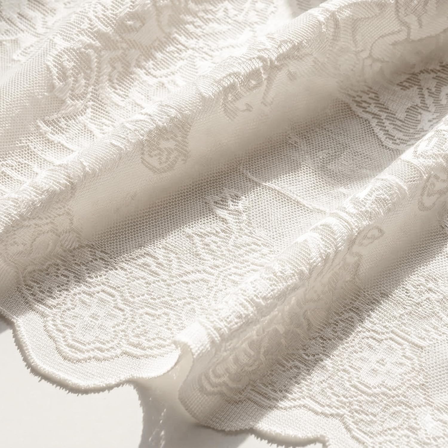 Close-up of elegant white sheer floral patterned lace fabric with a delicate scalloped edge, draped softly.