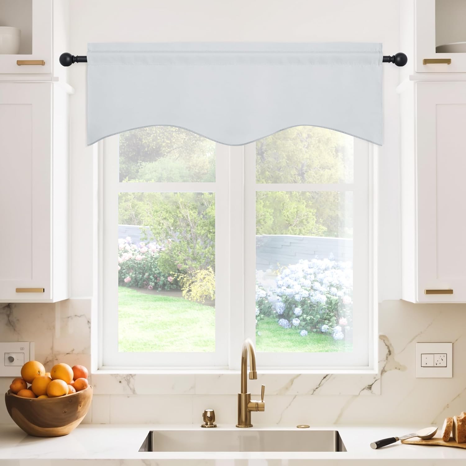 White scalloped valance curtain with rod pocket hangs on a black rod over a kitchen window.