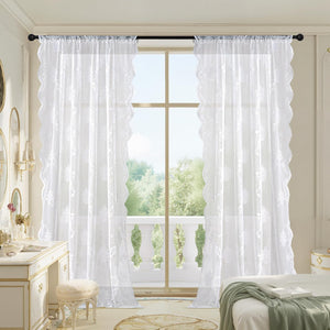 Elegant white sheer curtains featuring delicate floral lace embroidery and decorative scalloped edges, hanging in a bright bedroom.