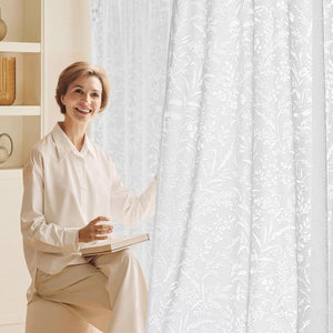 White sheer curtains with a detailed botanical lace pattern, gently filtering light in a bright room.