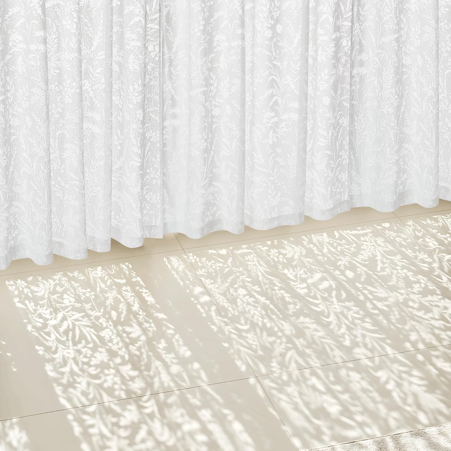 White sheer curtains with a delicate botanical pattern, filtering sunlight onto a light tiled floor.