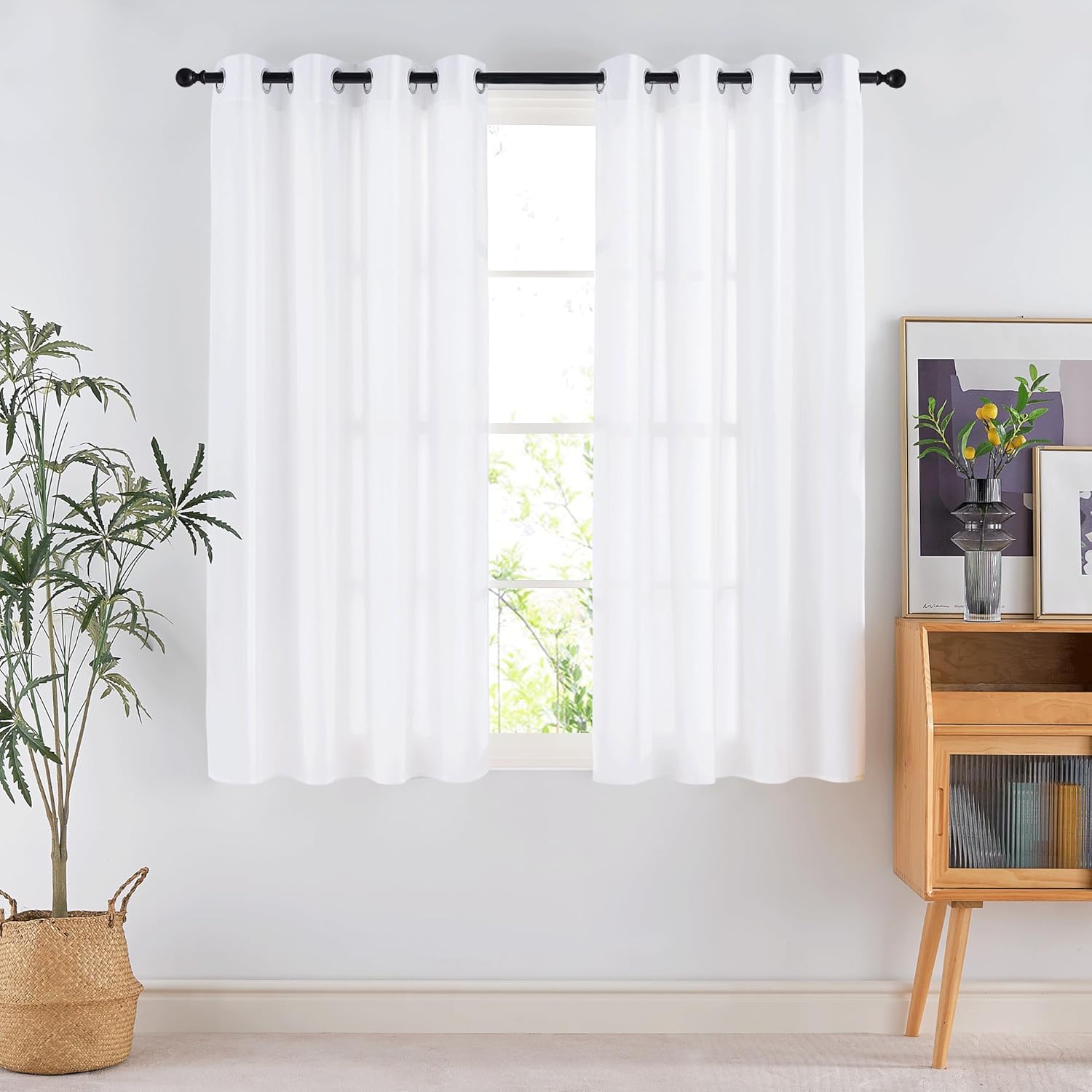 Two sheer white curtains with silver grommet tops on a black rod, filtering light through a window.