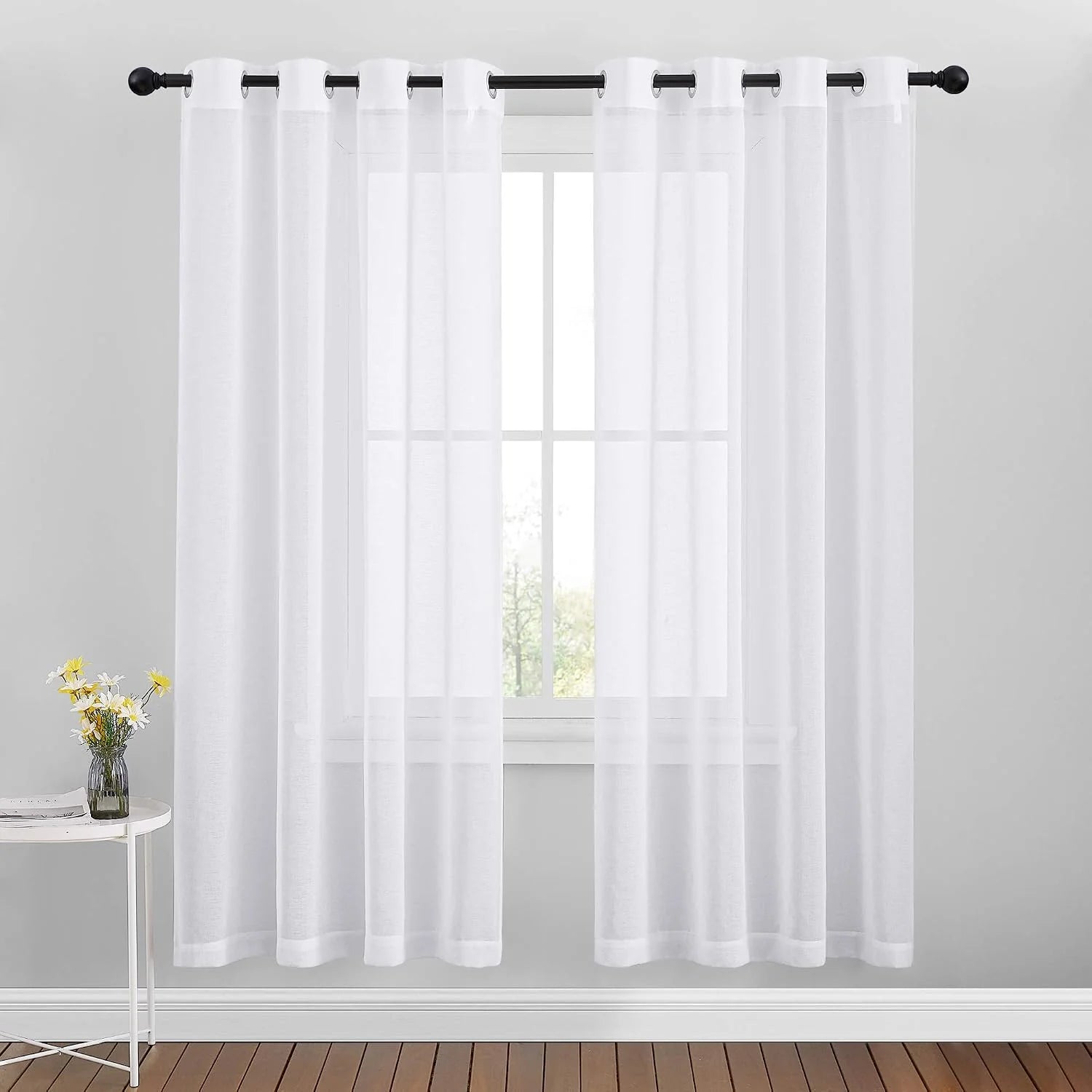 White sheer grommet curtains hanging on a black rod over a bright window