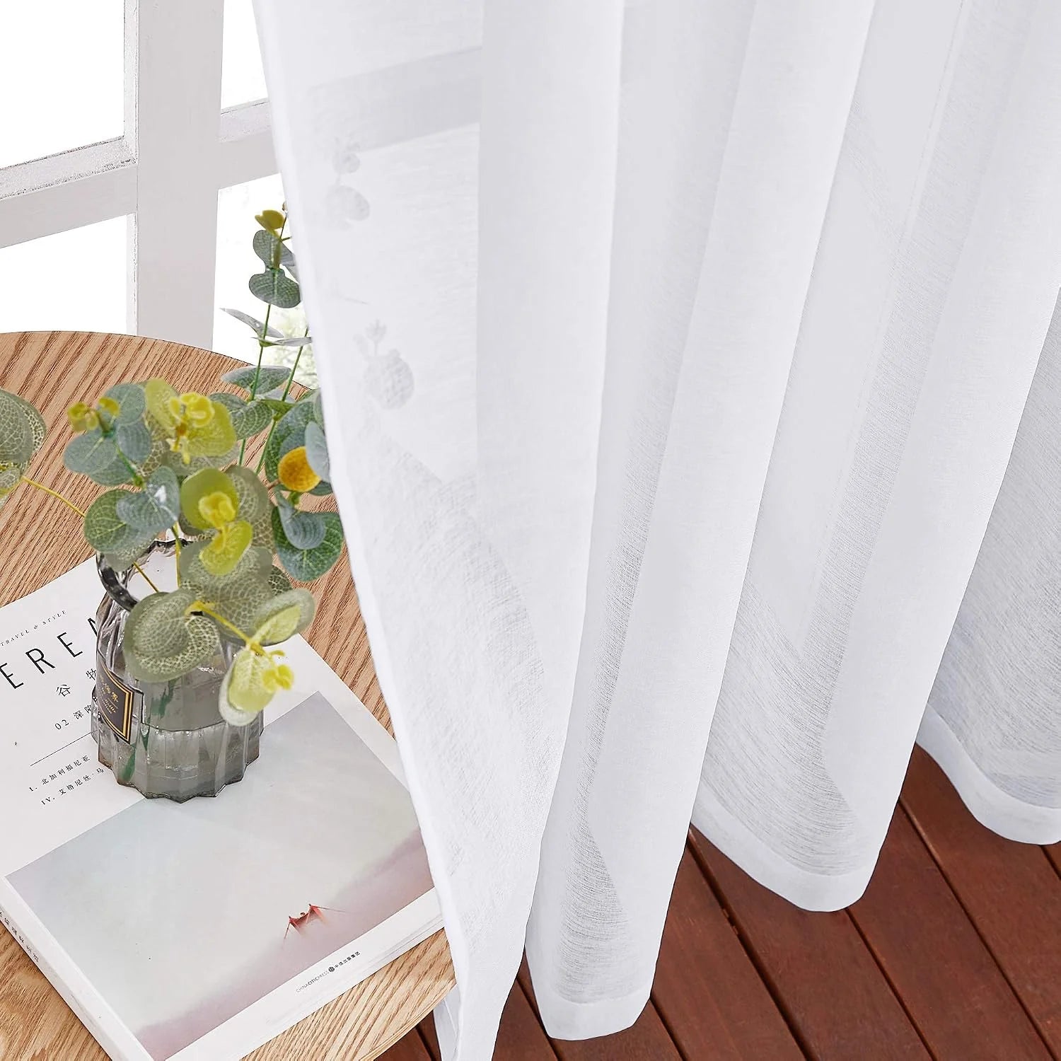 White sheer linen-look curtain draped by a window beside a wood table and vase