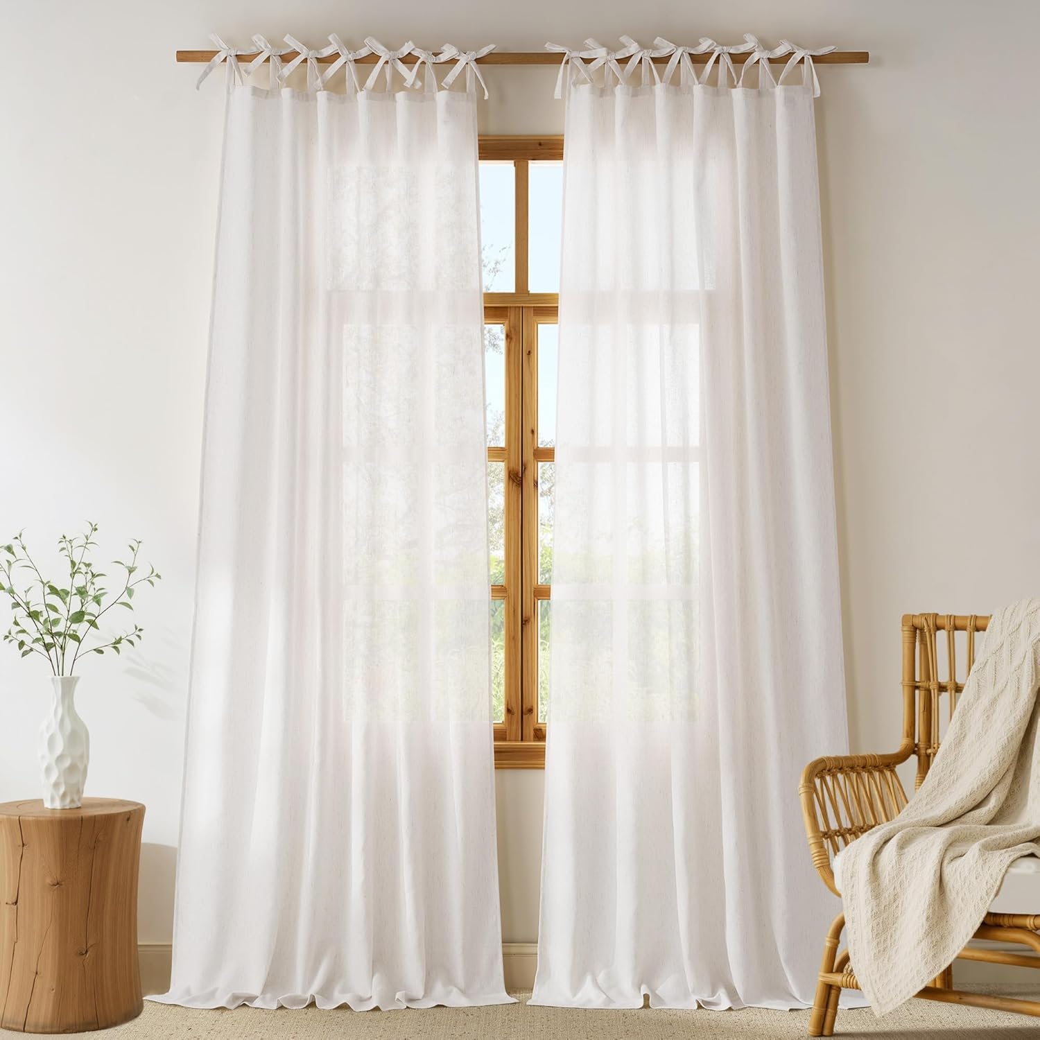 Pair of white sheer linen tie-top curtains hang on a wooden rod, softly diffusing light through a window.