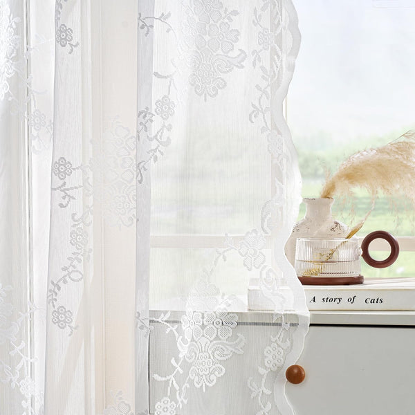 Elegant white sheer lace curtains with intricate floral embroidery and scalloped edges softly filter light.