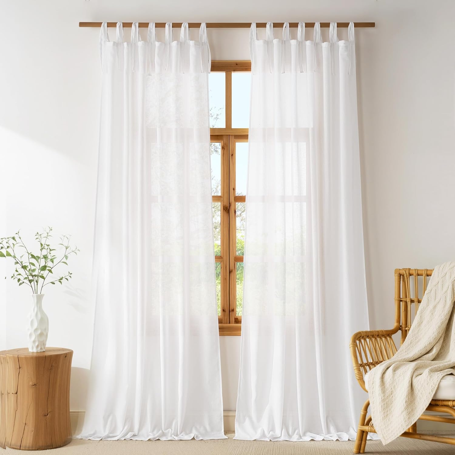 Two white sheer tie-top curtain panels hang elegantly from a wooden rod, letting light filter into the room.
