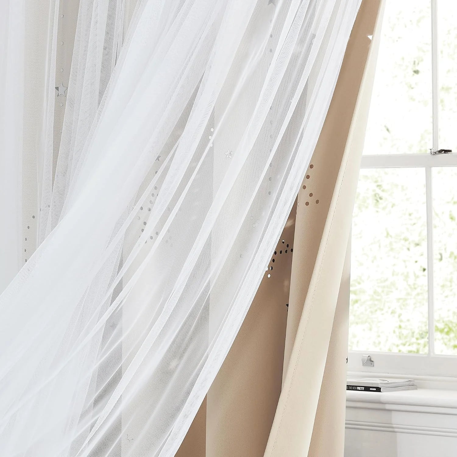 White sheer tulle canopy curtain draped beside a bright window in a soft bedroom