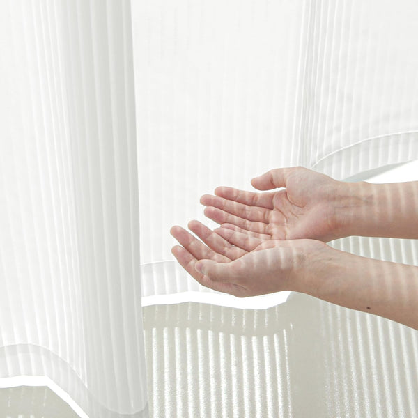 White sheer vertical pleated curtain with soft sunlight filtering through, casting striped shadows on cupped hands.