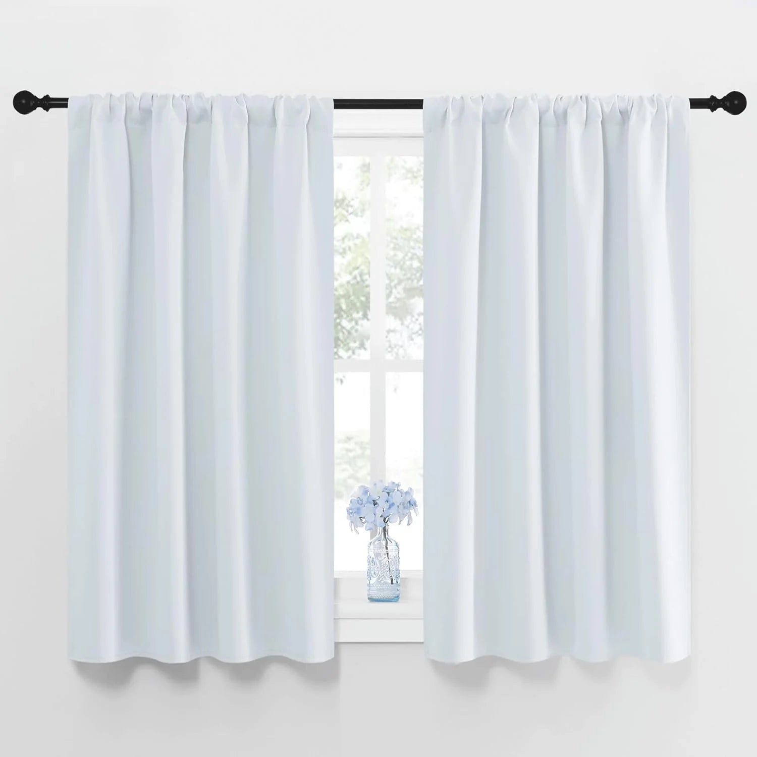 Pair of white rod pocket short curtains on black rod, windowsill with blue flowers.