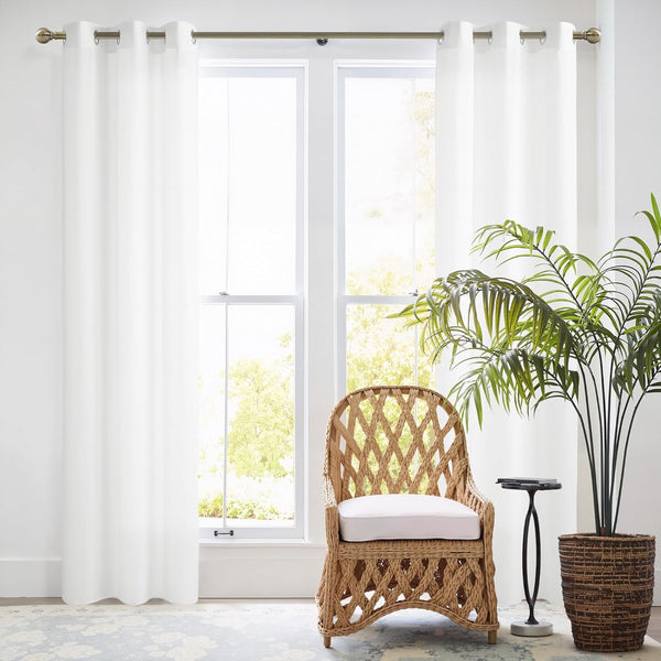 Bright white smooth curtains with metal grommets on a brass rod, framing a large window.