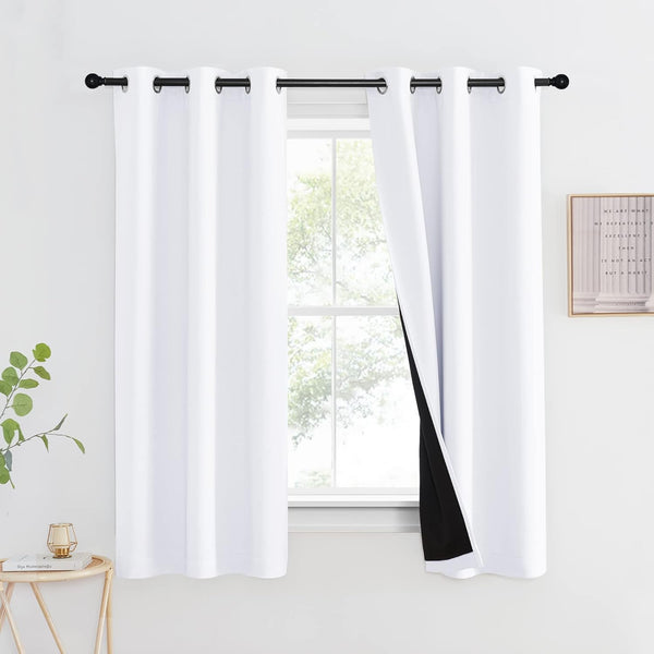 Pair of white solid blackout curtains with black grommets on a rod, one pulled back to show dark lining.