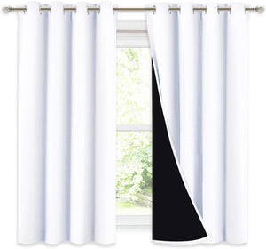White solid blackout curtain panels with metal grommets hanging on a window rod, revealing black lining.