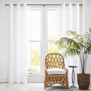 Crisp white solid curtains with bronze grommet tops hanging on a window rod in a bright living space.