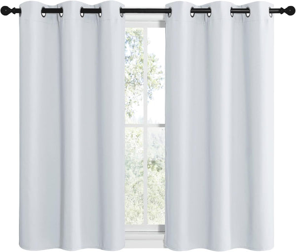 Two white solid blackout curtains with black grommet tops hanging on a black rod in front of a window.