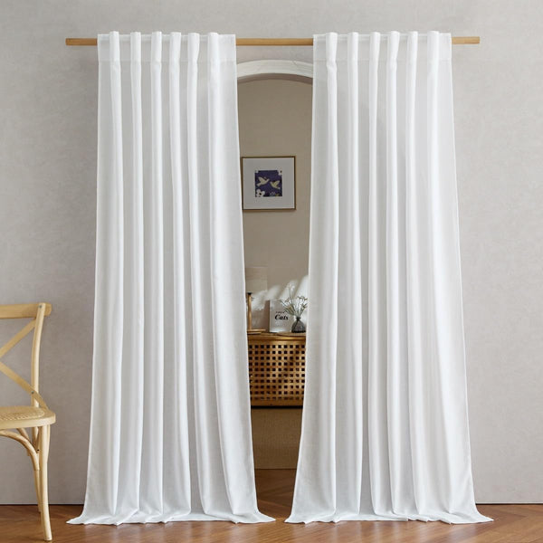White tab top linen blend curtains hanging on a wooden rod, gently pooling on a wooden floor.