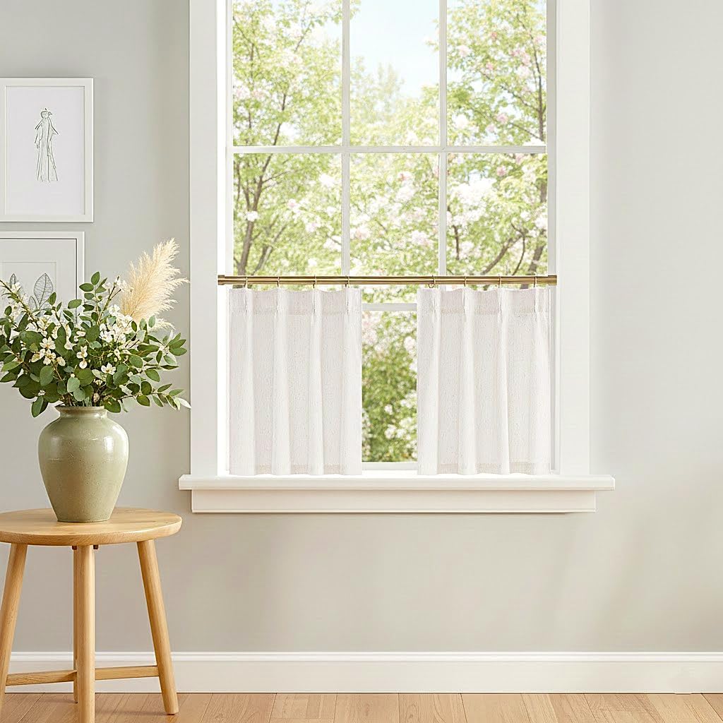 White textured sheer cafe tier curtains hung on a brass rod, allowing light to filter through a window.