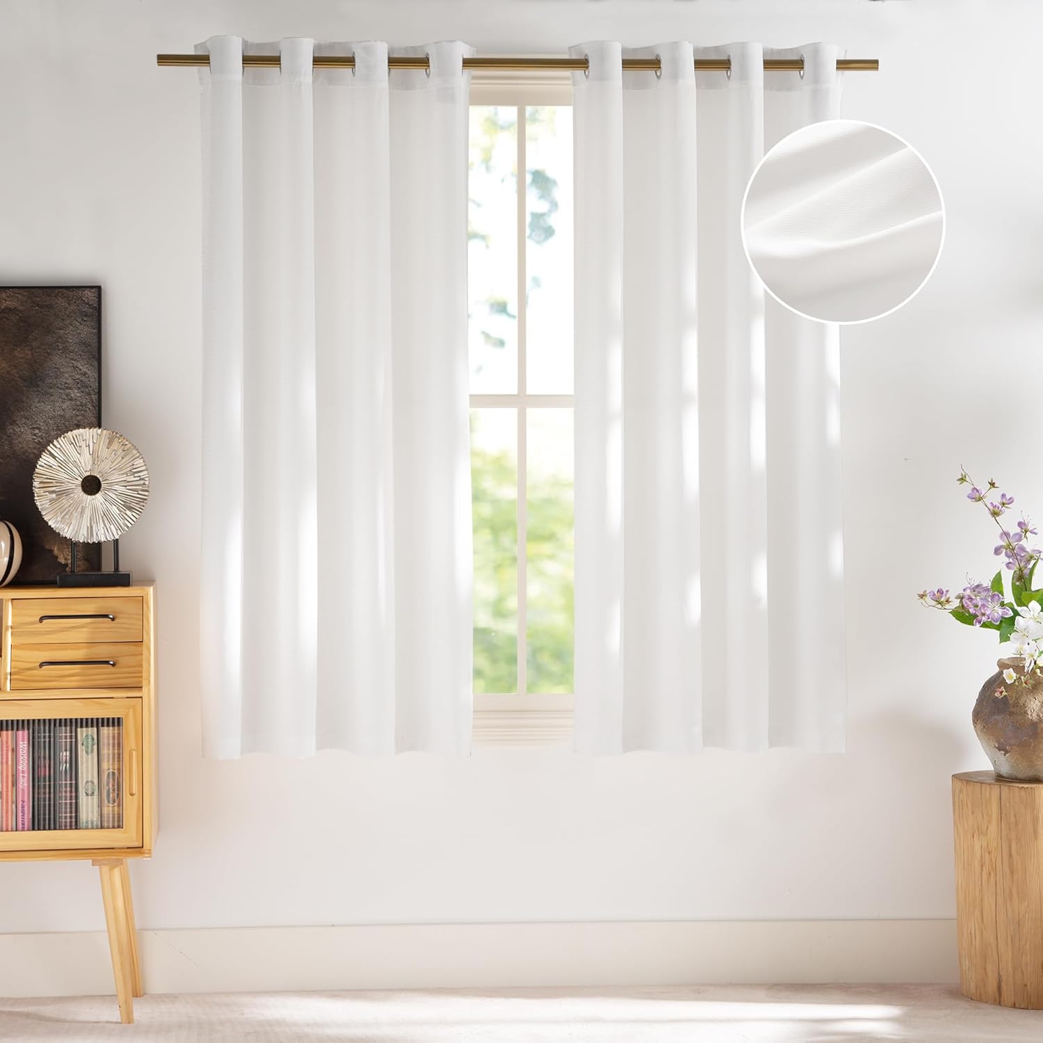 White textured semi-sheer grommet top window curtains hanging on a brass rod in a sunny room.