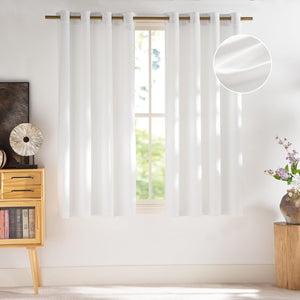 White textured semi-sheer grommet top window curtains hanging on a brass rod in a sunny room.