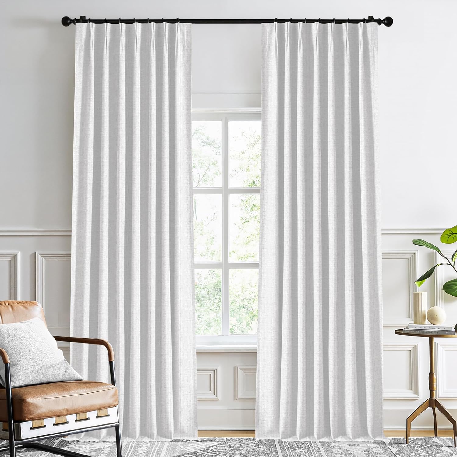 White textured fabric curtains with elegant pleats hanging from a black rod in a bright modern living room.