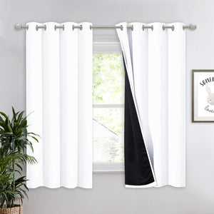 White thermal blackout curtains with silver grommets, showing a black lining, hung on a rod over a window.