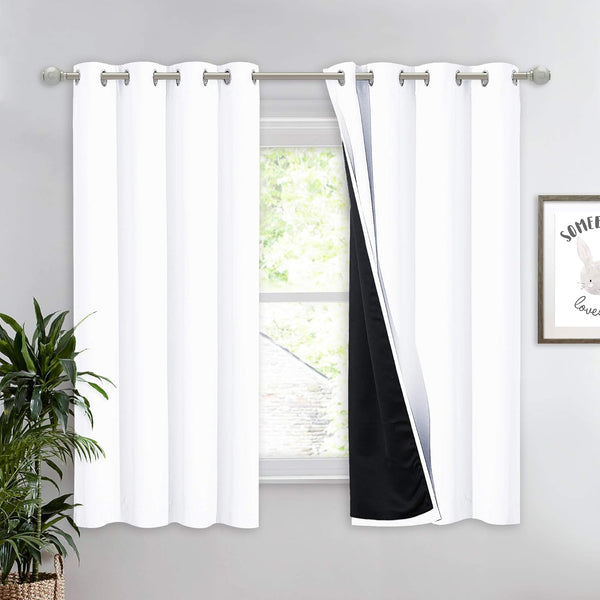 White thermal blackout curtains with silver grommets, showing a black lining, hung on a rod over a window.