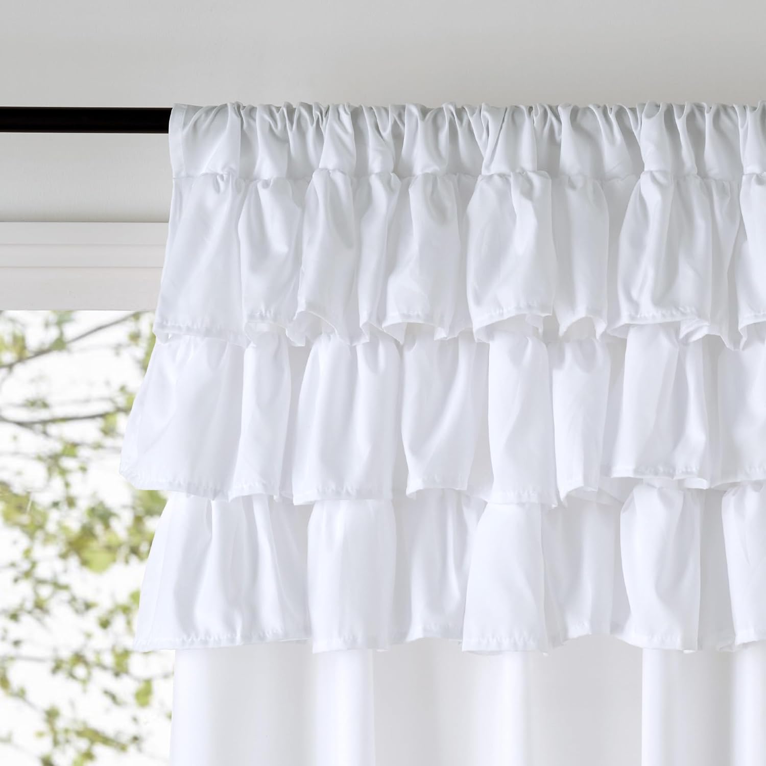 White tiered ruffled curtain panel with a gathered rod pocket top, hanging by a window.