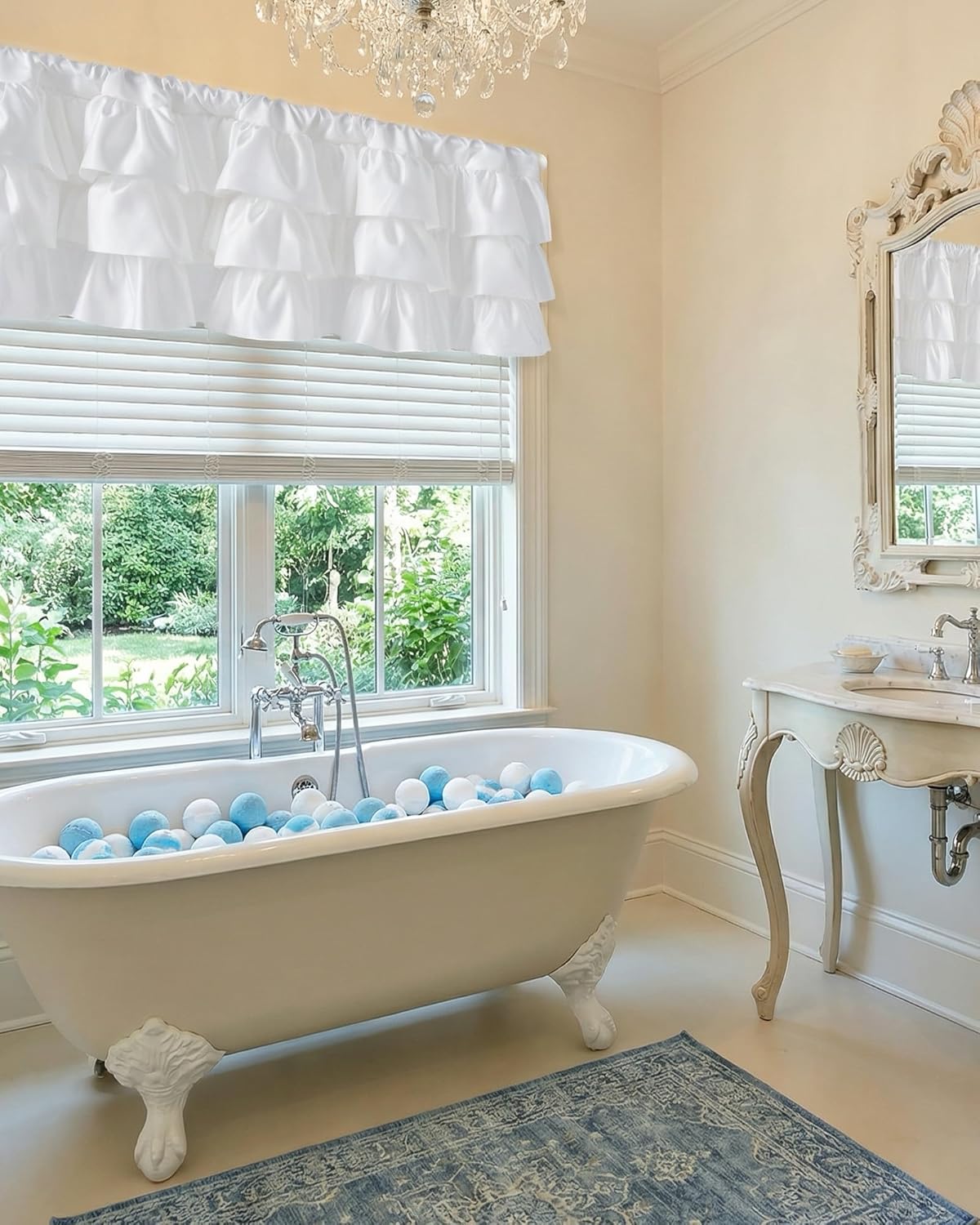 White tiered ruffled window valance hanging above horizontal blinds in an elegant bathroom with a clawfoot tub.