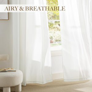 Airy white sheer curtains with subtle vertical stripes hanging in a bright, sunlit room.