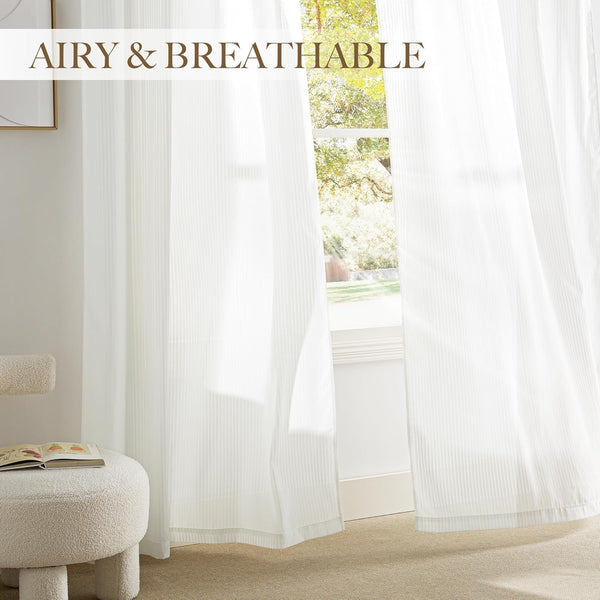 Airy white sheer curtains with subtle vertical stripes hanging in a bright, sunlit room.